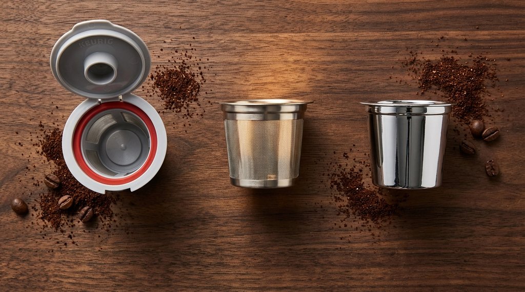 Three reusable K-Cup pods side by side on a wooden surface showing different designs